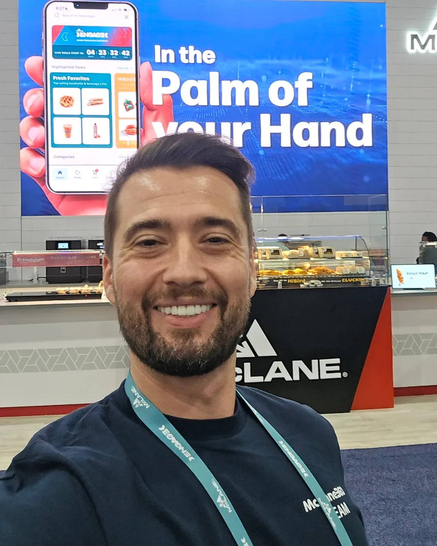 Erman Yaman on the Engage show floor with McLane360 displayed on the large screen behind him